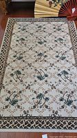 Large rectangular cream rug with palm tree and floral motif, bordered with geometric pattern