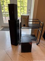 Two Sony speakers, Sony subwoofer, Koss subwoofer on rolling metal cart near door.
