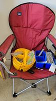 Red fabric folding camping chair holding yellow hardware organizer and blue container with nails and screws.