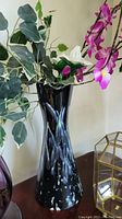Black and white speckled tall ceramic vase with faux flowers inside, shown against beige wall.