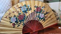 Front view of large decorative hand fan wall art showing floral paint design and wooden ribs