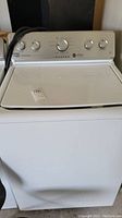 Front view of white Maytag top load washing machine with control panel and lid visible.