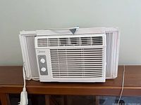 Front view of white Midea window air conditioner showing front grill, side accordion panels, and electrical cord.