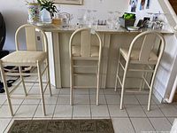 Front and side view of three cream-colored wooden barstools with fabric seats arranged in front of kitchen island, showing structure, backrest design, and upholstery.
