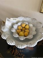 White ceramic bowls with scalloped edges, one nested inside the other, the smaller bowl containing faux yellow pears.