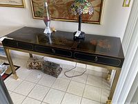 Full view of the black oriental-style console table showing eastern thematic artwork on top, three drawers, and metal legs, with objects placed on top.