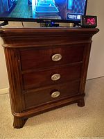 Front view showing three drawers with silver-tone oval handles and carved fluted vertical side detailing.