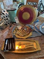 Overview photo showing the gold plated platters, decorative porcelain platter, mixed flatware on gold platters, and boxed rabbit handled spreaders.