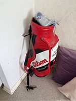Red, black and white Wilson FatShaft golf bag standing upright. Shows front side with Wilson logo and carrying strap.