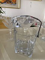 Image of the cut glass ice bucket with metal handle in front of four cut glass martini glasses