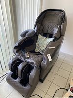 Front view of brown massage chair with remote in footrest compartment and blue decorative pillow on the seat.