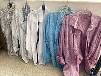 Five men's long sleeve shirts hung on plastic hangers, showing striped, solid, blue, and purple patterns