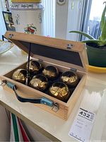 Open wooden case showing six solid metal bocce balls arranged in padded interior.