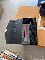 Photo of Audi branded red metallic microphone in black leather case with foam interior and coiled black cable.