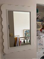 Full wall mirror mounted on wall showing scalloped white wooden frame with grooved inner border.