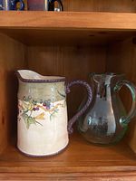 Wooden shelf holding two pitchers side by side: ceramic Tracy Porter pitcher with floral design and glass pitcher