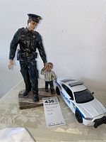 Policeman statue holding a child and white Florida police patrol car on table with lot number tag.