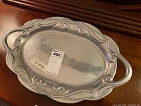 Full view of the silver platter showing overall shape, handles, and decorative rim.