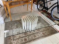 Full view of the glass coffee table showing clear glass top and marble base on a patterned rug.