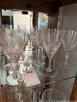 Photo showing 11 cut glass wine and cordial glasses on a glass shelf with a label.