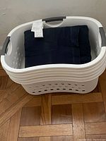 Three white and gray plastic laundry baskets stacked inside each other, with one basket containing folded dark clothing.