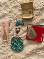 Photo showing assorted jewelry items spread on fabric: turquoise stone coin purse, keychain, brooch, earrings box, metal pendant, cloth pouch.