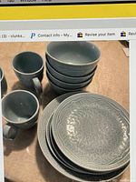 Photo of four stacked gray ceramic bowls and two gray ceramic mugs with embossed geometric patterns on their surfaces.