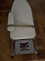 Ironing board with attached sleeve board and metal iron rest on wheeled legs on a wood floor.