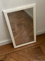 Medium-sized rectangular mirror leaning against a wall on a wooden floor, showing frame details and mirror condition.