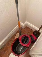 Oval floor cleaning pail and mop leaning against wall on wooden floor