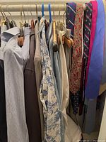 Hanging men's ties alongside shirts and jackets on a rack, showcasing the ties' designs and colors.