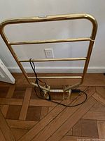 Gold-tone electric towel drying rack showing three horizontal bars, power cord and control switch on base.