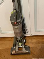 Photo of an upright Hoover Air wet carpet cleaning machine showing the front dirt container, handle, and power cord with signs of dirt and wear on the brush base.