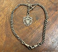 Full view of the entire sterling silver watch chain and attached fob laid flat on a wooden surface.