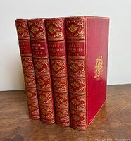 Four red leather-bound books standing upright showing spines and front cover of last volume