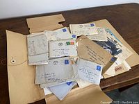 Photo showing multiple vintage envelopes and handwritten letters arranged on a wooden surface along with some photo prints.