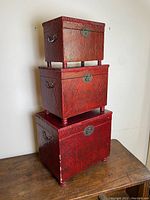 Three red rectangular Chinese stacking boxes with metal lock plates and side handles stacked on top of each other showing general shape, color, and condition.