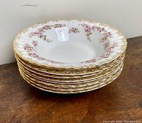 Stack of 8 bone china soup bowls with decorated rim showing gold and pink rose pattern.