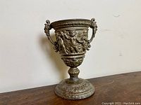 Full side view of the cast metal chalice showing two handles, pedestal base, and relief cherub decorations