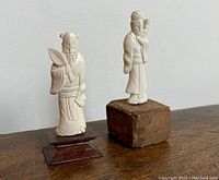 Both hand carved Chinese figures on teakwood bases side by side on a wooden surface