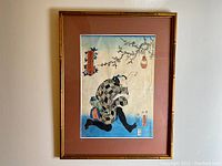 Full view of framed Kunitada woodblock print mounted on wall, showing the entire artwork with bamboo-style frame and reddish brown mat.