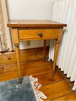 Front view of antique pine candle table showing single drawer with round knob and turned legs on pine wood floor.