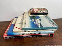 Stacked books on Japanese art showing spines and covers including Hokusai's Mount Fuji, Japanese Graphic Art, The Grammar of Japanese Ornament, and others.
