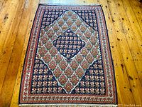 Full view of the hand woven Persian carpet laid flat on a wooden floor showing the geometric and floral patterned design with dominant blue and red tones.
