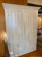 Front view of the white painted antique pine armoire showing two paneled doors and the wide top molding.