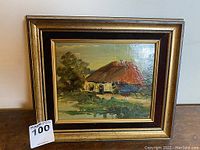 Front view of the framed original oil on canvas painting showing a thatched roof cottage with surrounding greenery and water reflection.