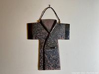 Front view of pottery wall hanging shaped like a kimono with textured surface and hanging wire.