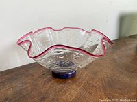 Overview of the glass bowl showing its clear glass body with bubble inclusions, ruffled pink-edged rim, and purple base.