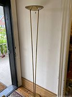 Full view of the vintage brass torchiere lamp standing near a doorway, showing its height and design.