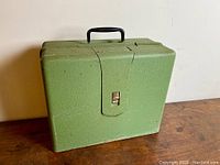 Closed green textured metal carrying case with black handle, showing front latch and overall condition.